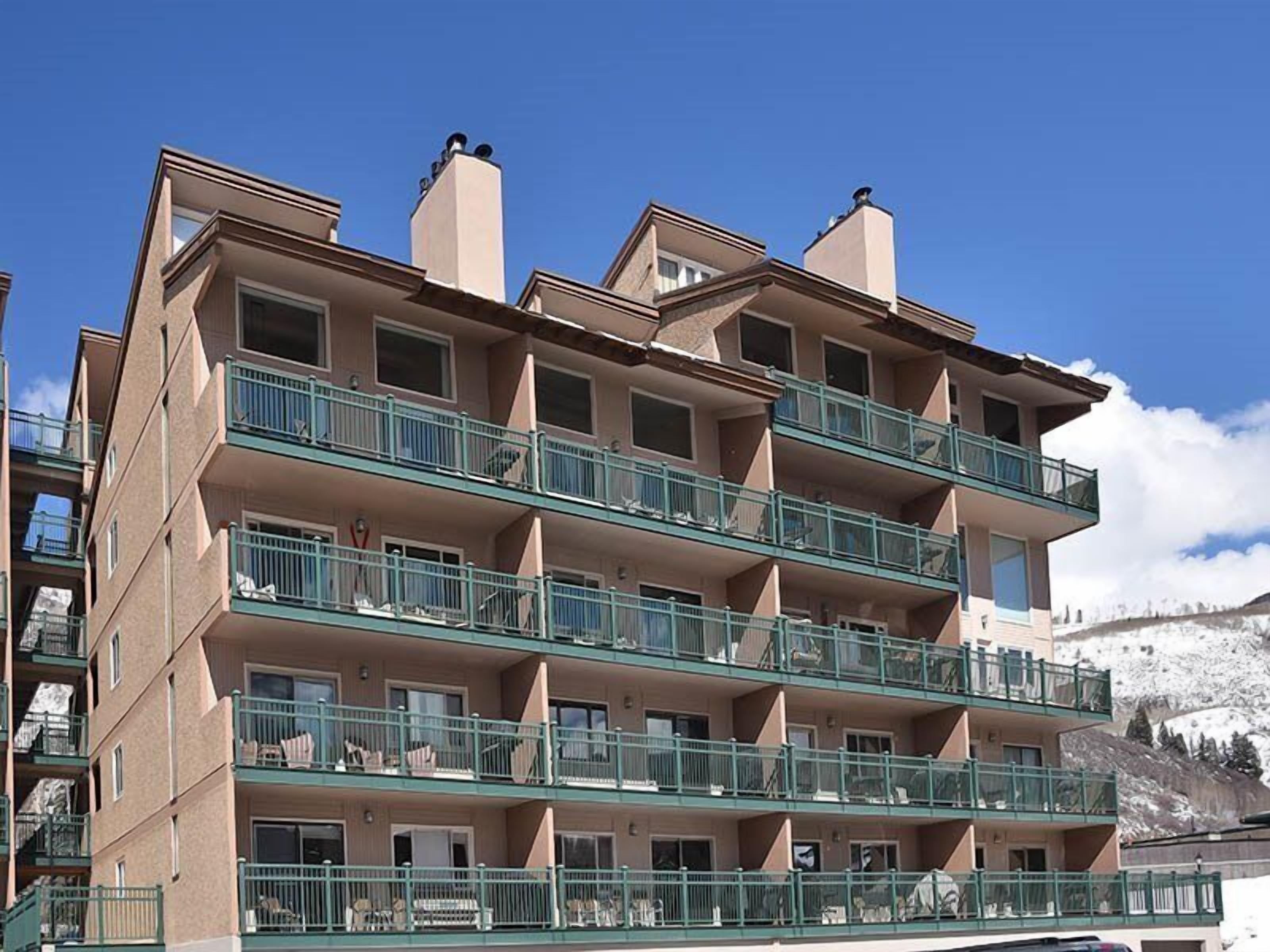 Un hôtel à plusieurs étages, doté de balcons, d’un toit plat et situé dans un cadre montagneux.