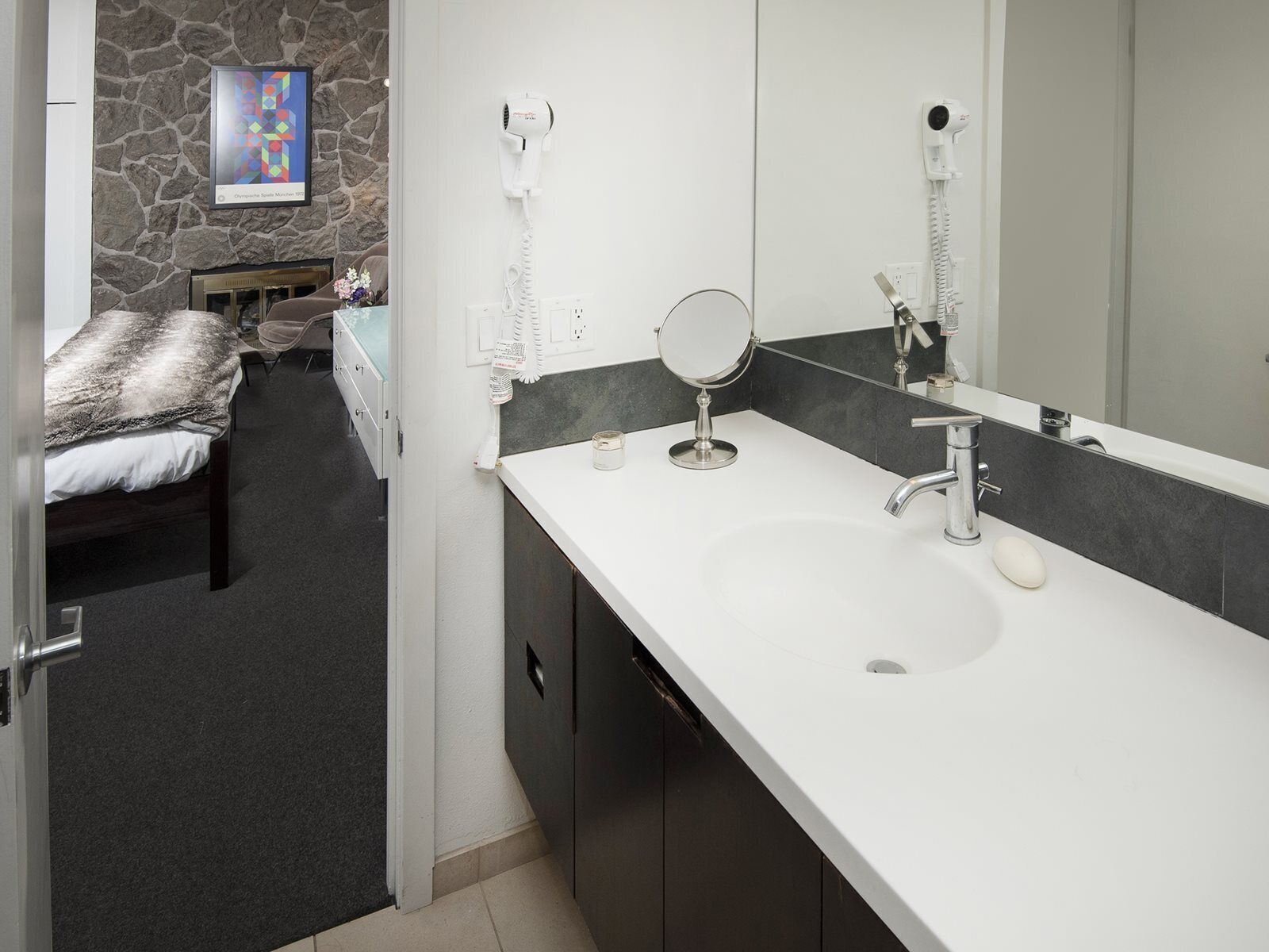 A modern bathroom with a white sink, a large mirror, and a hairdryer mounted on the wall.
