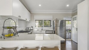 Een moderne keuken met witte kasten, een centraal eiland met krukken, een roestvrijstalen koelkast en een raam dat voor natuurlijk licht zorgt.
