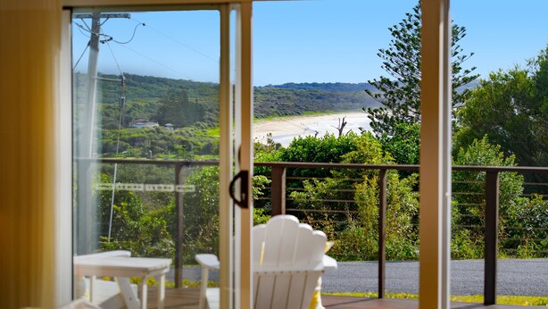 Een balkon met een witte stoel en tafel, met uitzicht op een strand en begroeiing.