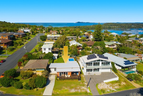 An aerial view of a residential area with houses, a road, and a large body of water in the background.