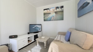 A living room with a flat-screen TV, a white entertainment unit, a beige sofa, and a patterned rug.