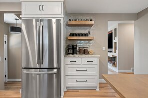 Une cuisine moderne dotée d’un réfrigérateur en acier inoxydable, de meubles blancs, d’un coin café et d’un aquarium intégré.
