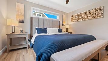 Un dormitorio con cama, mesitas de noche, un banco, ventilador de techo y obras de arte en las paredes.