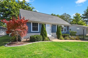 A single-story house with a grey shingle roof, a front porch, and a well-maintained lawn.