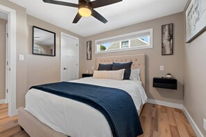 A bedroom with a bed, a ceiling fan, a window, and a wall-mounted shelf.