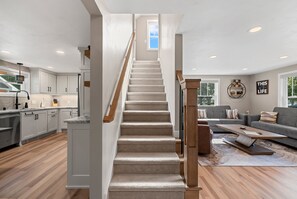 Un intérieur moderne avec un escalier menant à un deuxième étage, une cuisine dotée de meubles blancs et un espace de vie comprenant un canapé et une table basse.