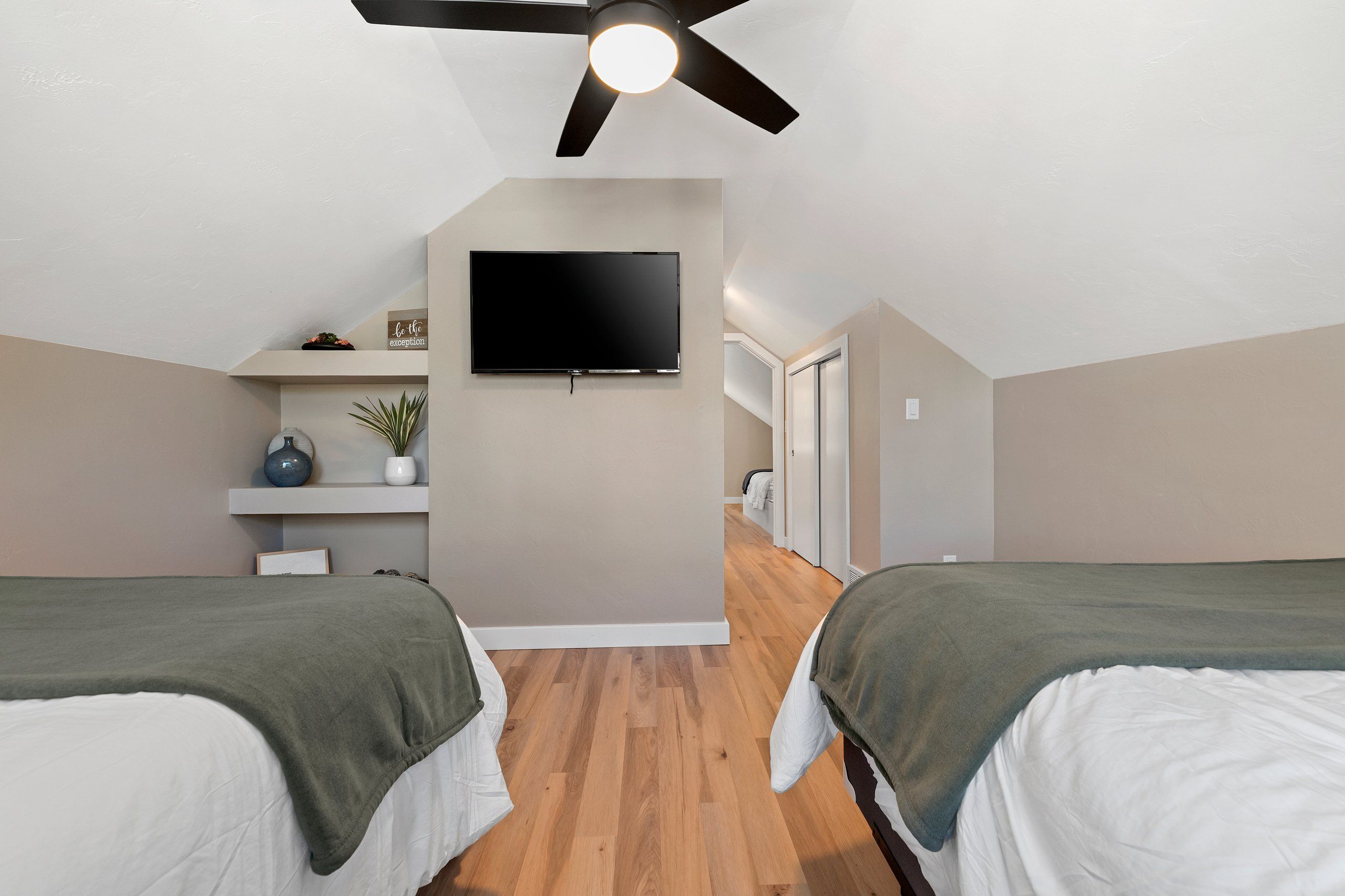 A bedroom with two beds, a ceiling fan, a TV, and a small shelf with decorative items.