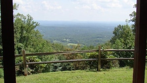 Une vue depuis une pièce dont la rambarde est en bois, donnant sur un paysage verdoyant et des montagnes lointaines.