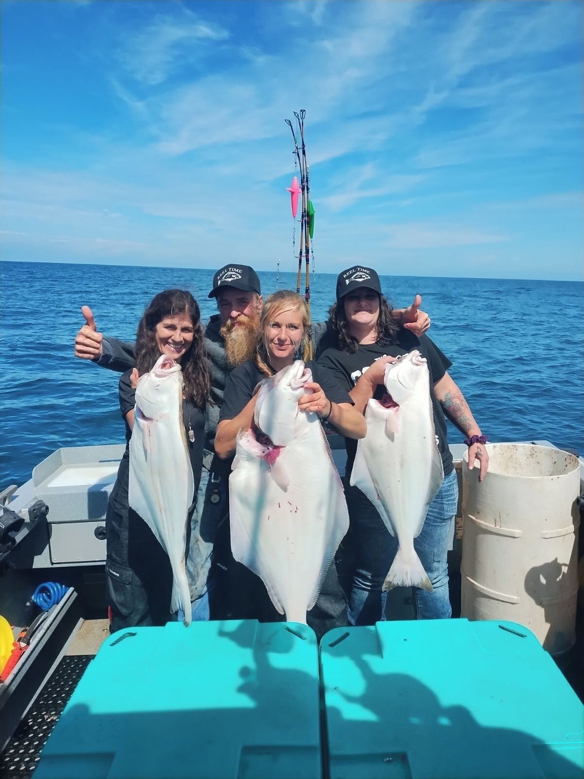 A group of people on a boat holding large fish, with a clear view of the ocean and a fishing rod in the background.