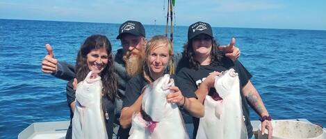 A group of people on a boat holding large fish, with a clear view of the ocean and a fishing rod in the background.