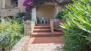 A stone building with a staircase leading to a covered entrance, surrounded by lush greenery and flowering plants. - Apartment  Trudi by Interhome (Cannigione)