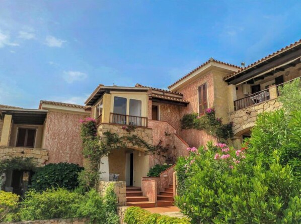 A multi-story house with a stone facade, a balcony, and a staircase leading to the entrance.