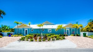 Un bâtiment à deux étages, doté d’une façade bleue, d’une entrée centrale et d’un jardin aménagé avec des plantes tropicales.