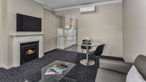 A modern living room with a fireplace, a flat-screen TV, a glass coffee table, and a dining area with a glass table and chairs. - Aloha Central Premium Studios (Mount Gambier)