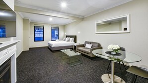 A hotel room with a bed, a sofa, a glass dining table, a TV, and a large mirror. - Aloha Central Premium Studios (Mount Gambier)