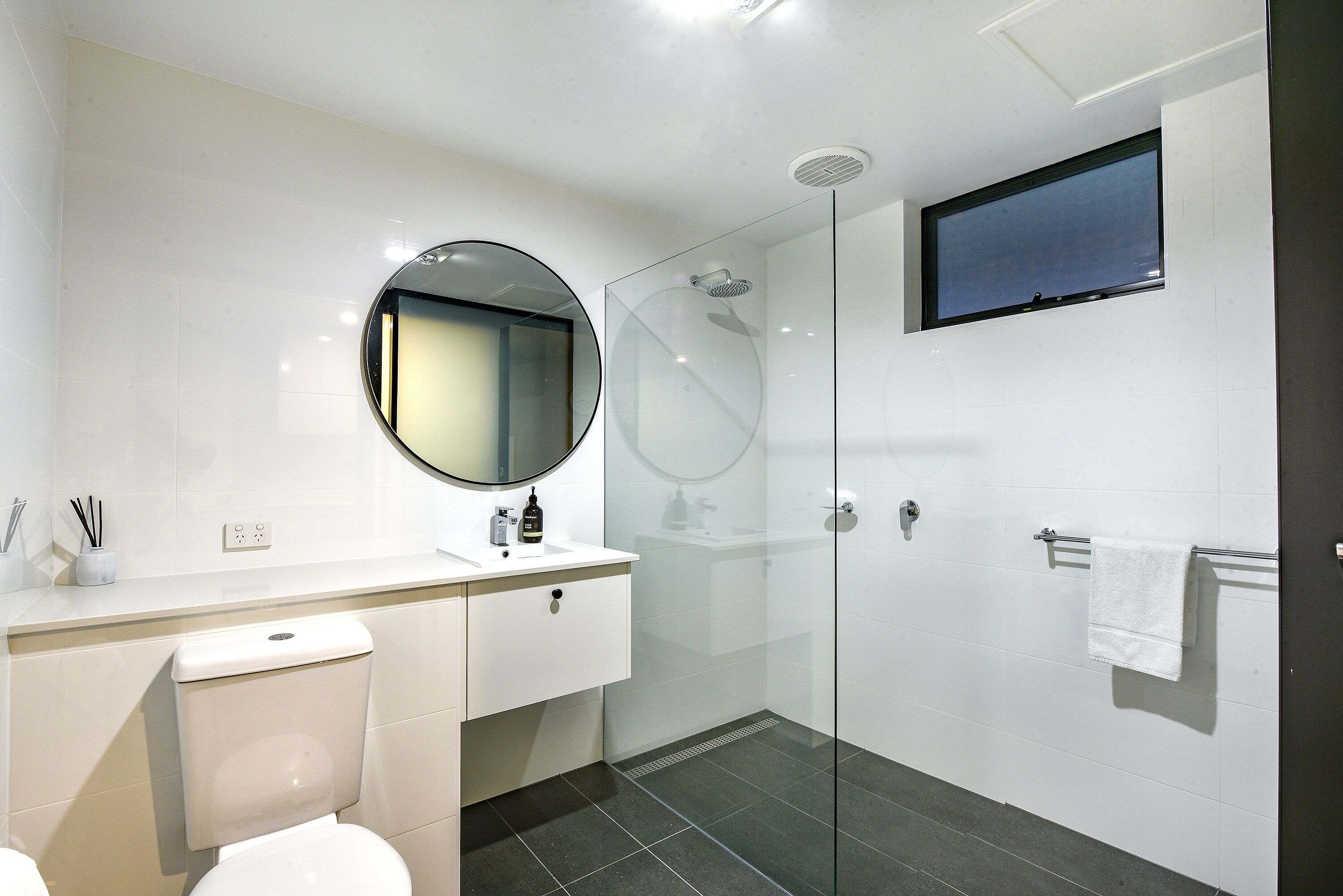 A modern bathroom with a toilet, sink, mirror, and glass-enclosed shower.