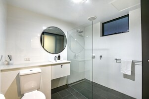 A modern bathroom with a toilet, sink, mirror, and glass-enclosed shower.