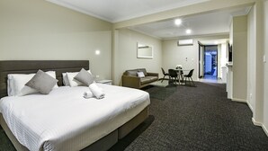 A hotel room with a large bed, a sofa, a dining area, and a TV. - Aloha Central Premium Studios (Mount Gambier)