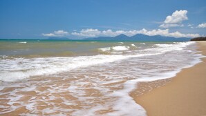 Una playa con olas, cielo despejado y montañas a lo lejos.