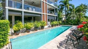 Un edificio moderno de dos pisos con piscina, plantas en macetas y mobiliario exterior.