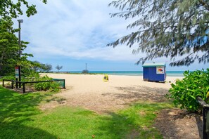 A beach with a blue portable toilet, a yellow sign, and a beach entrance gate. - Beachfront Apartment with Ocean Views (Yorkeys Knob)