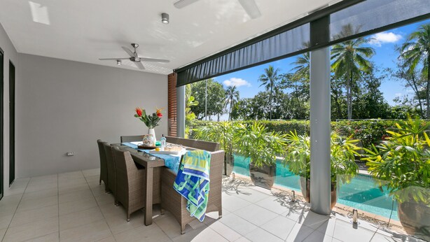 Un comedor moderno con una mesa y sillas, un ventilador de techo y vistas a una piscina y vegetación tropical.