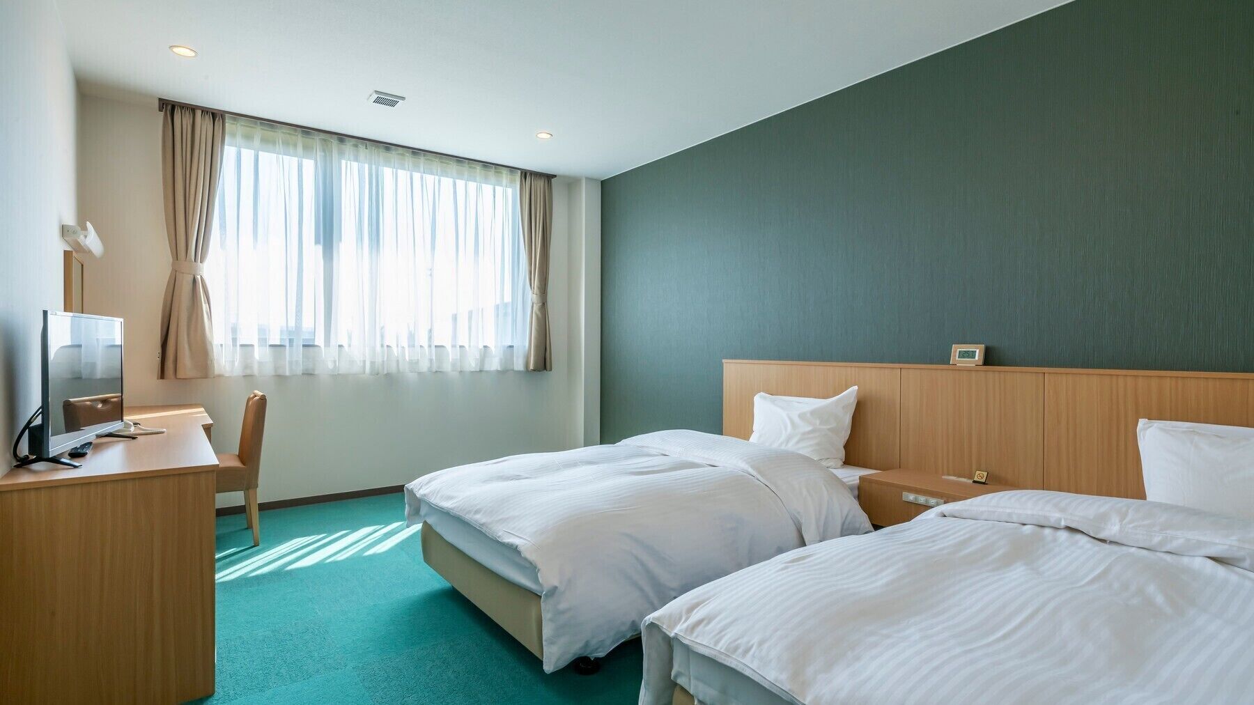 A hotel room with two beds, a desk, a chair, and a television.