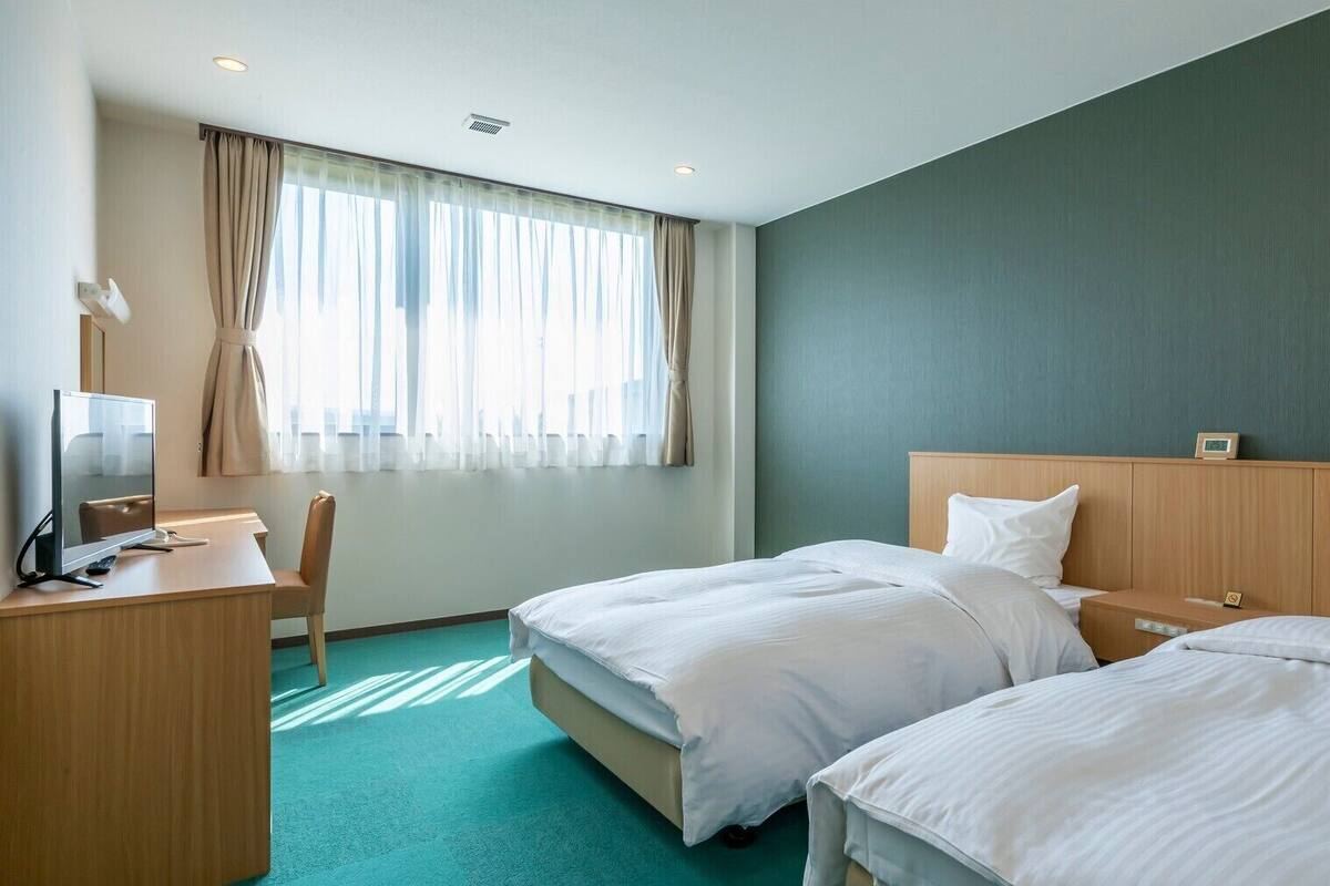 Quarto de hotel com duas camas, uma escrivaninha, uma cadeira e uma televisão.