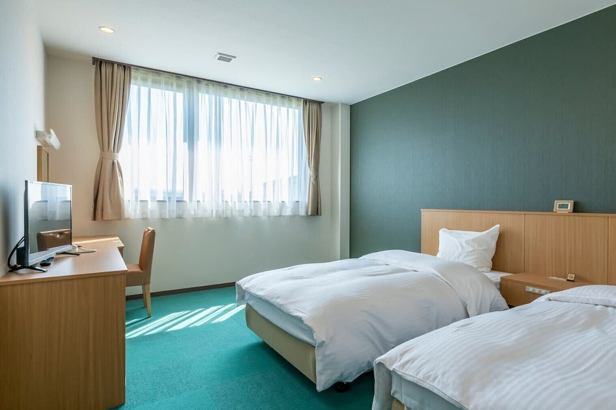 A hotel room with two beds, a desk, a chair, and a television.