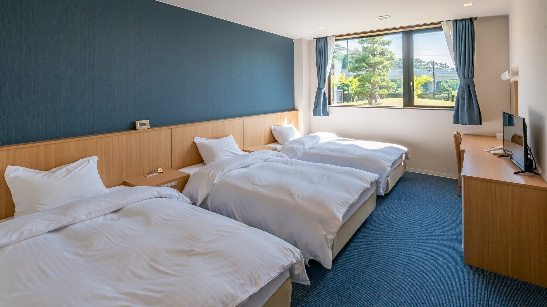 A hotel room with two beds, a desk, a TV, and a window with curtains.