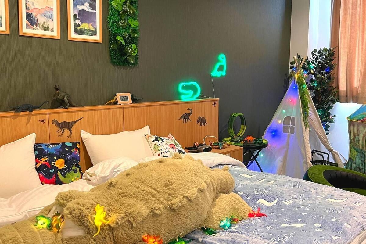 Quarto de criança com cama, decoração de dinossauros, uma tenda e um relógio.
