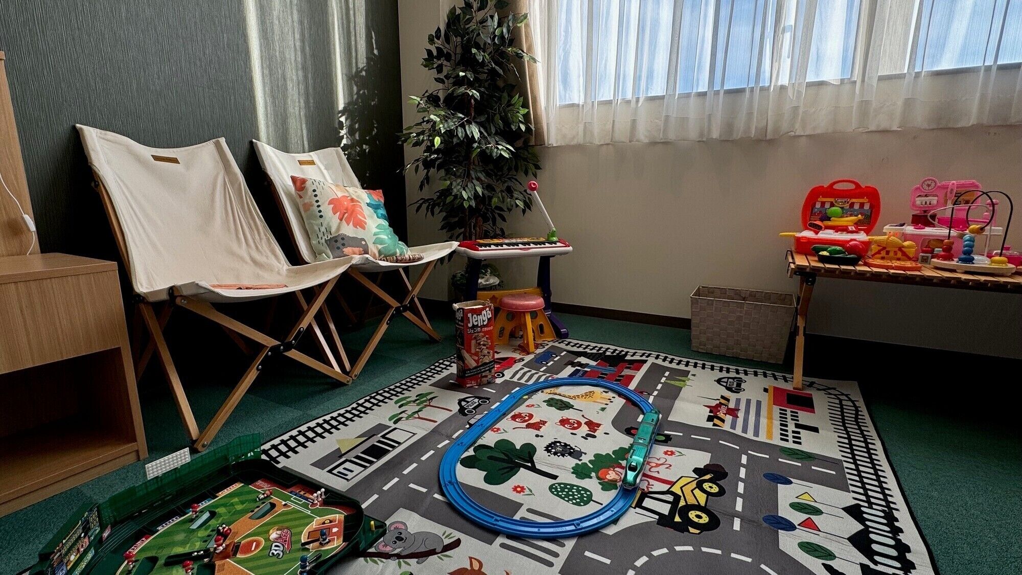 A room with two chairs, a small table with toys, a plant, and a colorful play mat.