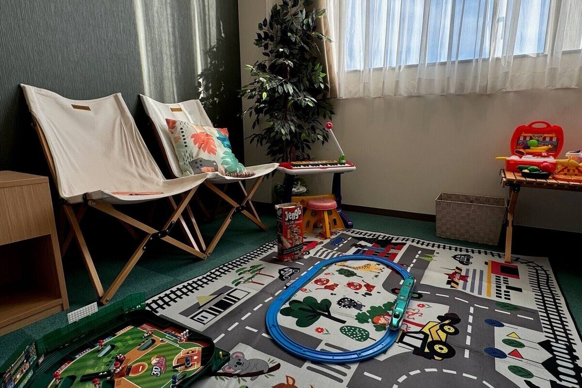 Um quarto com duas cadeiras, uma mesinha com brinquedos, uma planta e um tapete de atividades colorido.