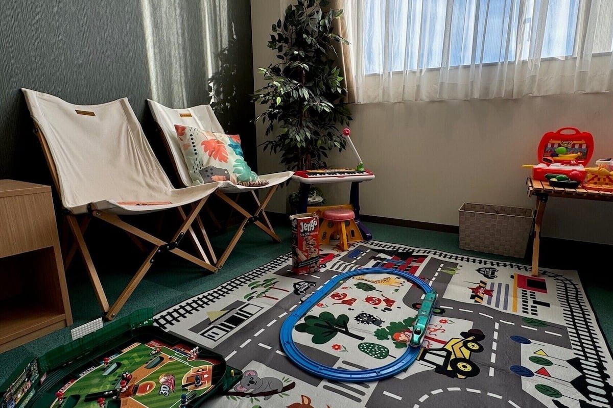A room with two chairs, a small table with toys, a plant, and a colorful play mat.