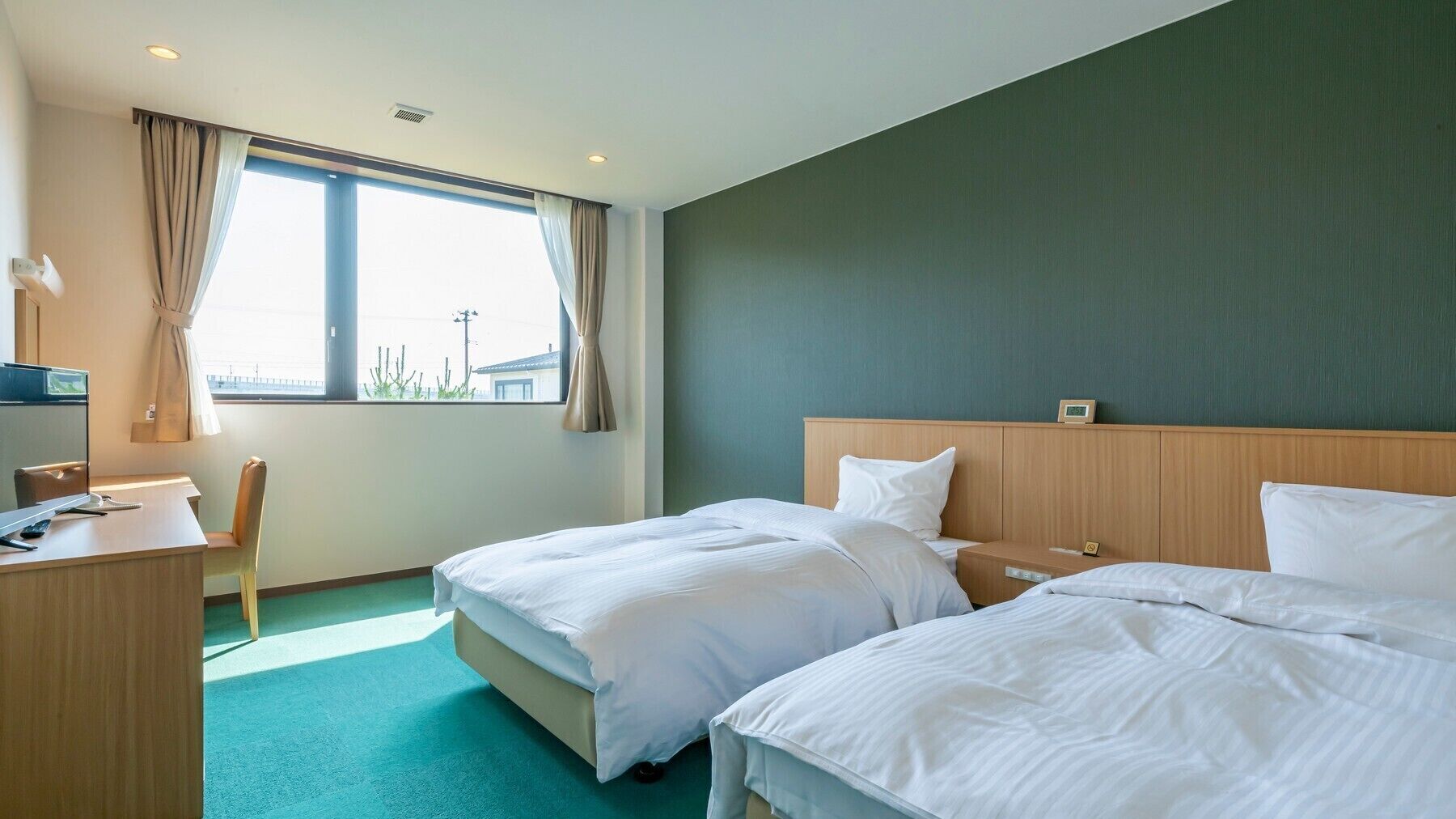 A hotel room with two beds, a desk, a chair, and a window with curtains.