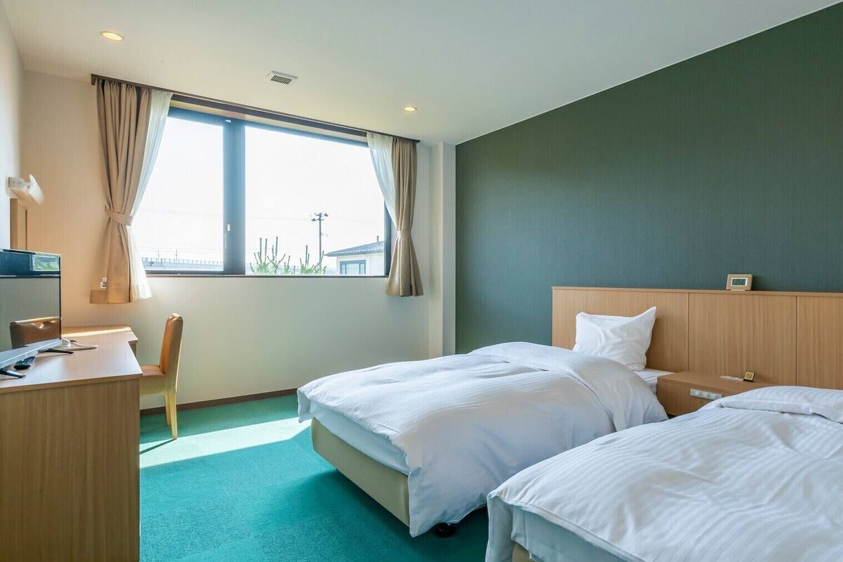 Quarto de hotel com duas camas, uma mesa, uma cadeira e uma janela com cortinas.