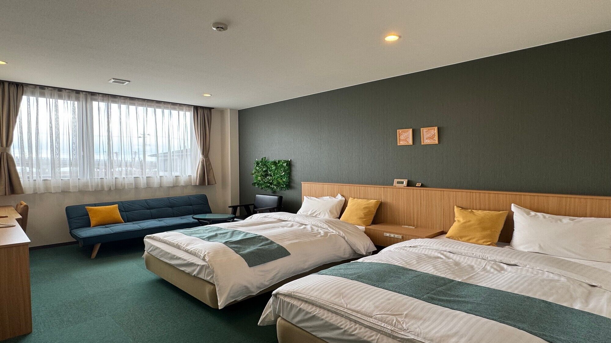 A hotel room with two beds, a sofa, a desk, and a view of the city.