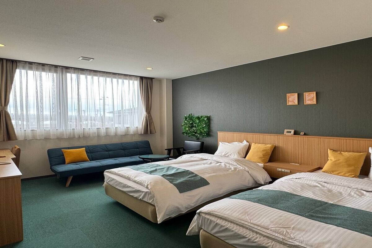 Quarto de hotel com duas camas, um sofá, uma escrivaninha e vista para a cidade.