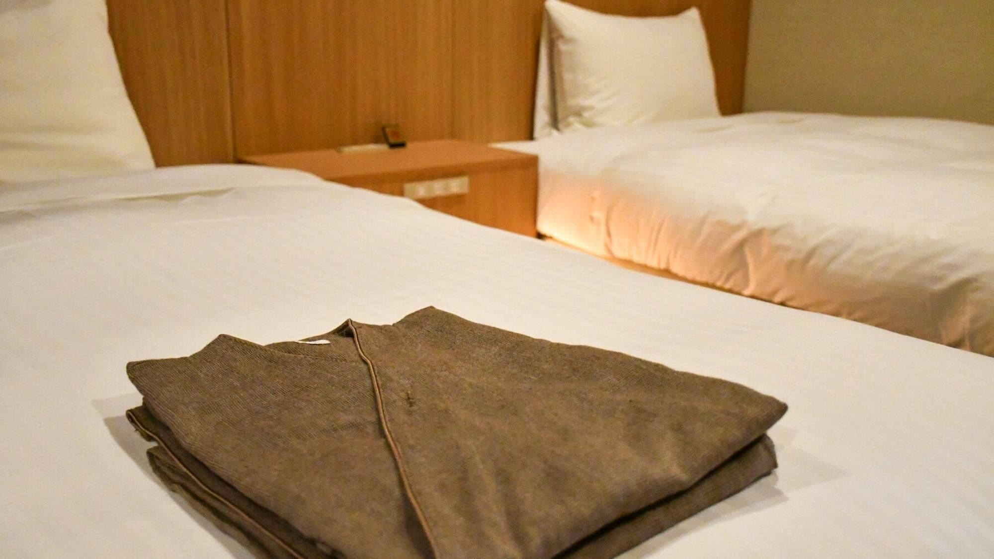 A neatly made bed with a folded brown garment on it, a wooden headboard, and a nightstand with a lamp.