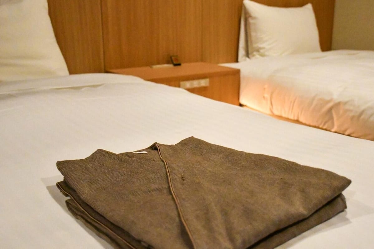 Uma cama bem arrumada com uma peça de roupa marrom dobrada sobre ela, cabeceira de madeira e uma mesa de cabeceira com abajur.