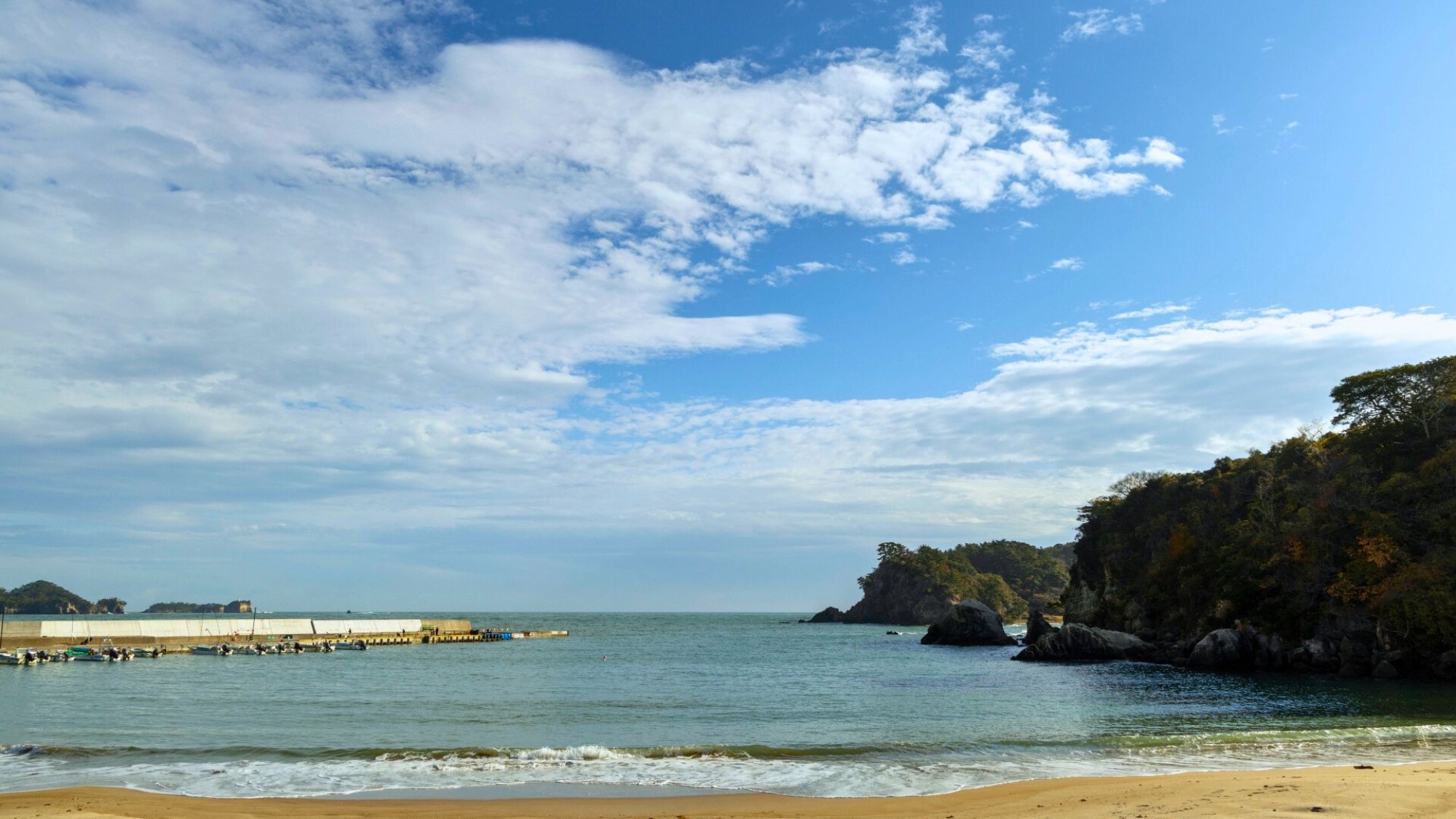 A beach with clear skies, calm water, and rocky cliffs.