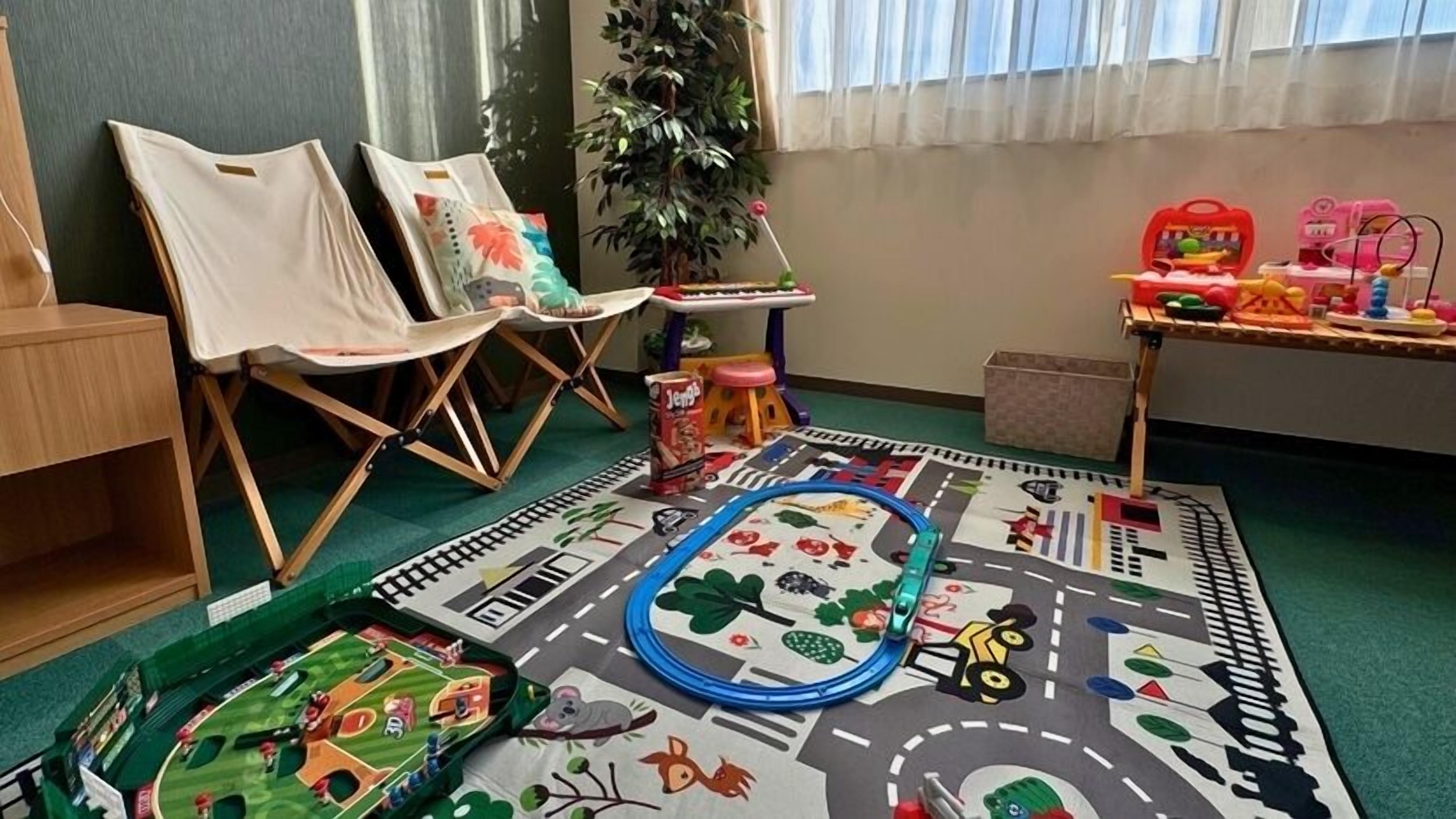 A playroom with a carpeted floor, chairs, a toy train set, and a small table with toys.