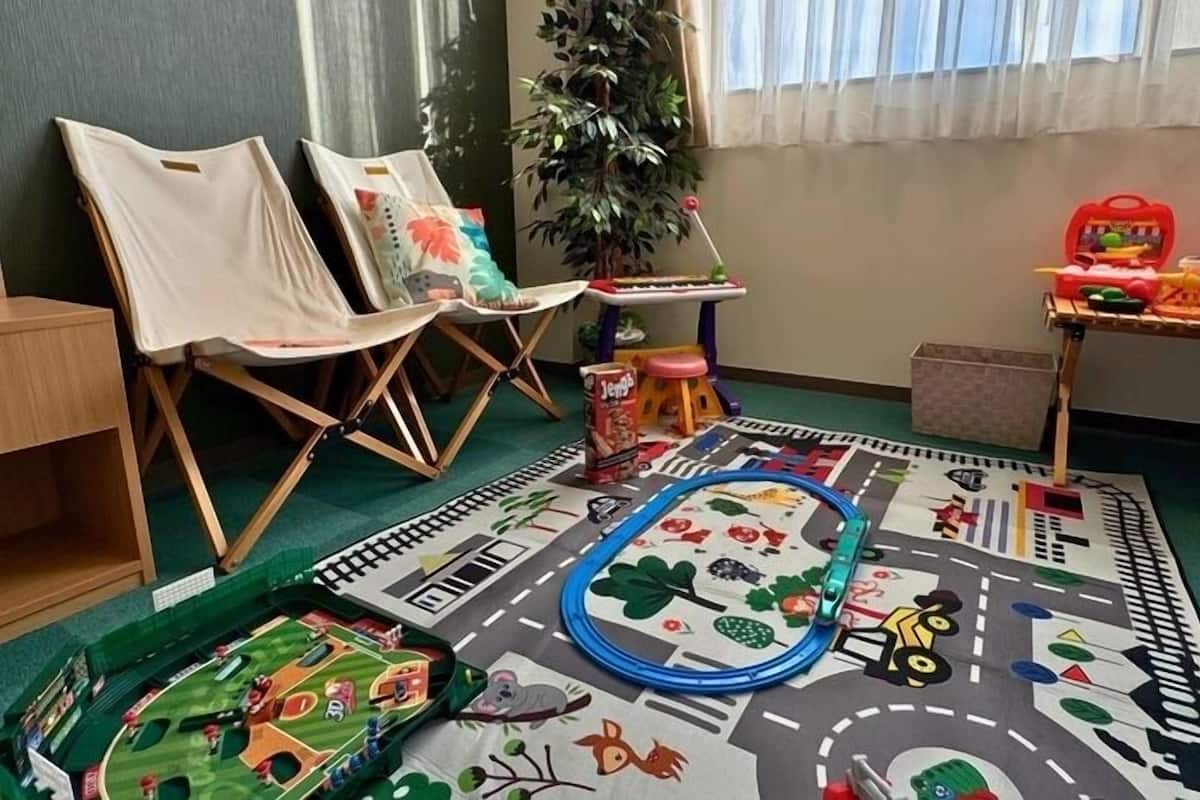 Una sala de juegos con piso alfombrado, sillas, un tren de juguete y una mesita llena de juguetes.