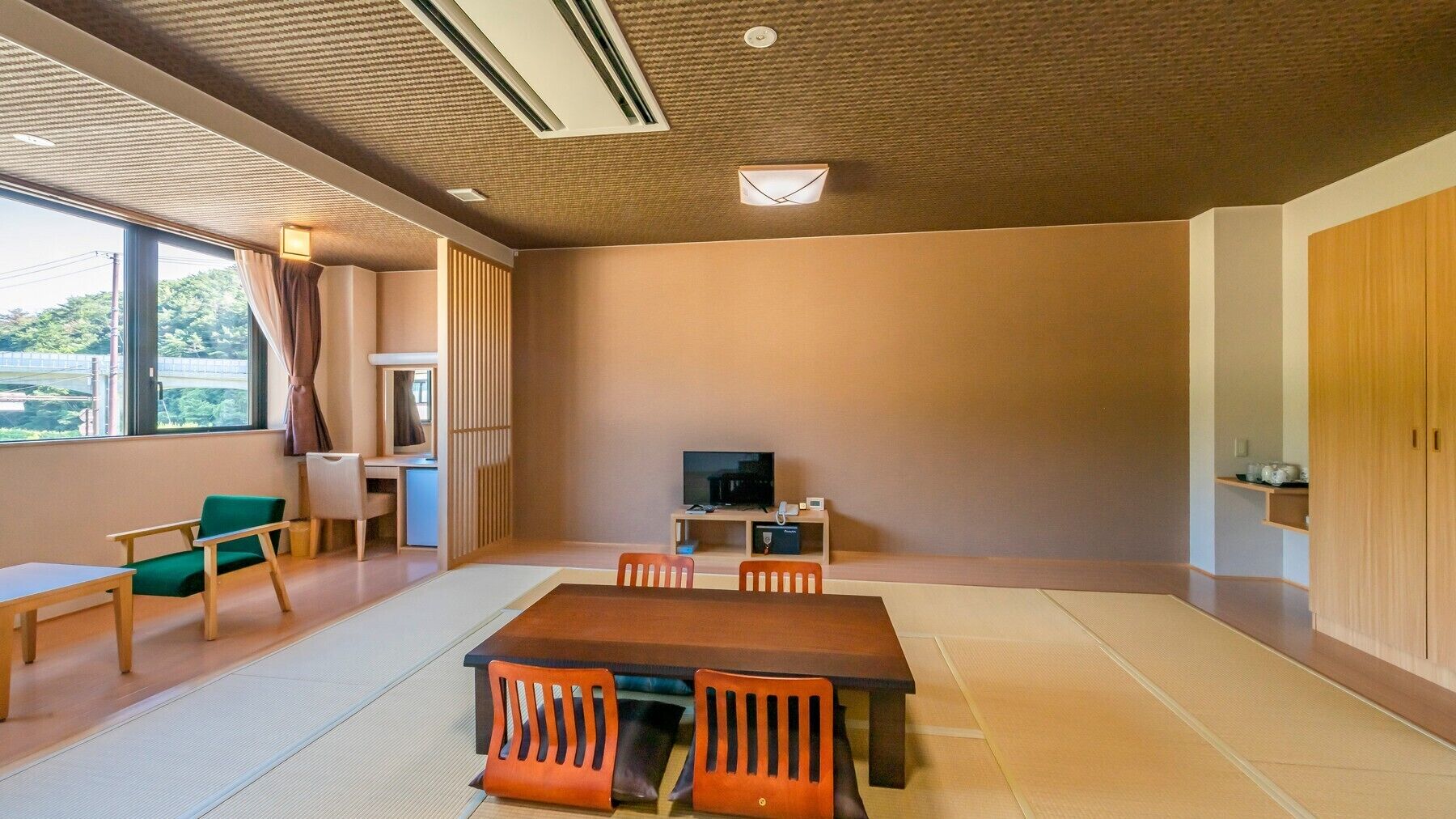 A room with tatami flooring, a low table, and chairs, a television, a desk with a computer, and a window with curtains.