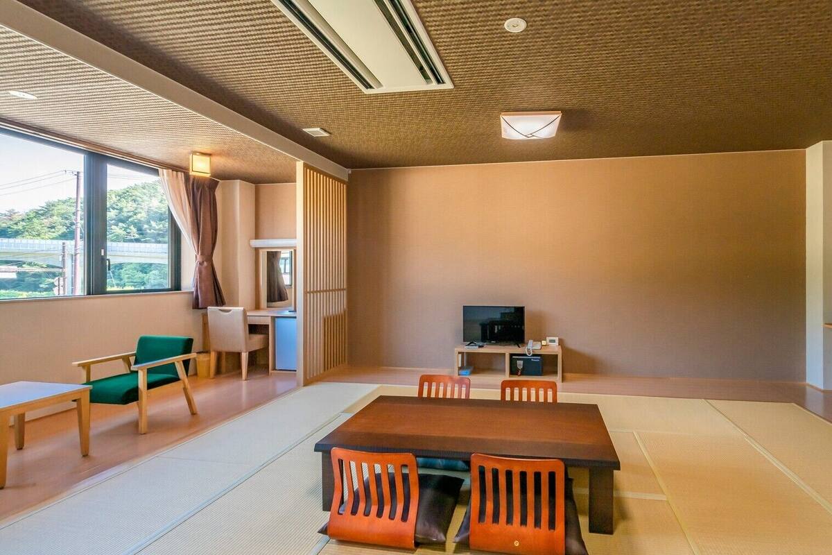 Quarto com tatames, uma mesa baixa e cadeiras, televisão, escrivaninha com computador e janela com cortinas.