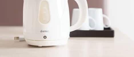 Una tetera eléctrica blanca sobre una mesa con una bandeja negra que sostiene dos tazas blancas.