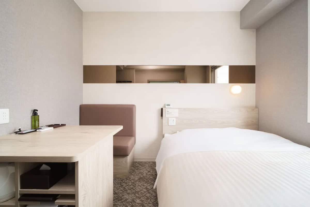 A hotel room with a bed, a desk, a chair, a mirror, and a nightstand.