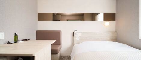 A hotel room with a bed, a desk, a chair, a mirror, and a nightstand.