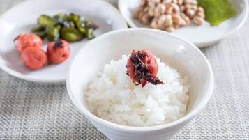 Un tazón de arroz blanco con una fruta roja encima, acompañado de un plato de verduras verdes y un plato de nueces.